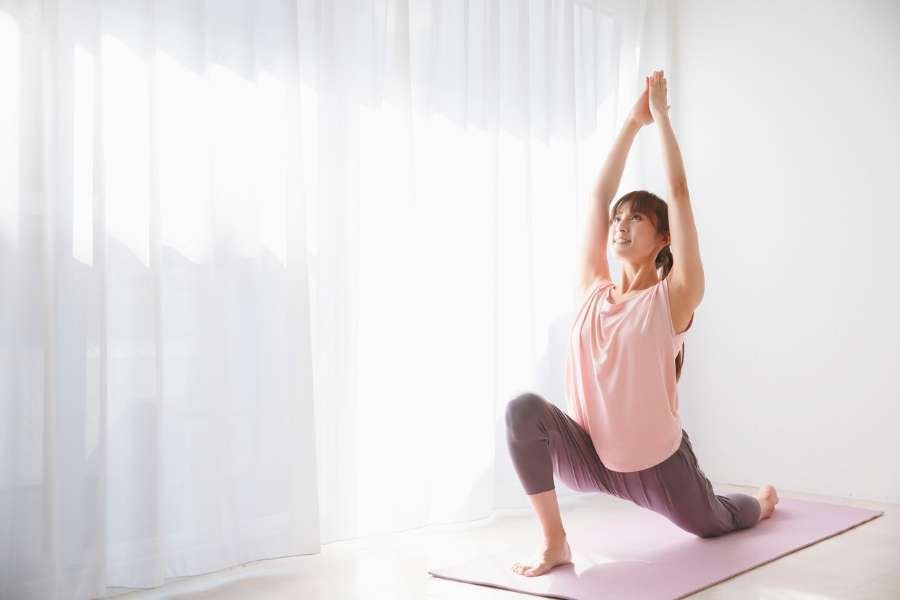 Une femme en fente avant sur un tapis rose pratique une des postures de yoga pour l'ouverture des hanches.