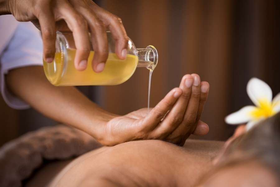 Un praticien verse des huiles de massage depuis un flacon en verre directement dans ses mains avant un soin du dos.